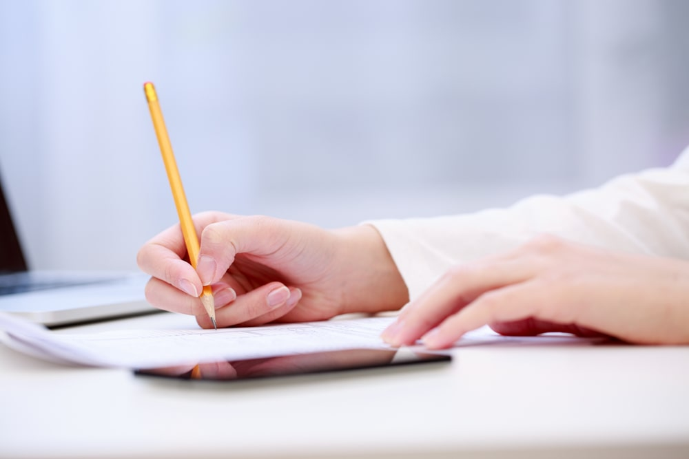 Infoprodutos: Como Transformar Seu Conhecimento em Renda 3 Pessoa anotando informações em um caderno ao lado de um laptop aberto com uma loja digital na tela. Criar infoprodutos demanda planejamento e estratégia para oferecer conteúdos de valor.