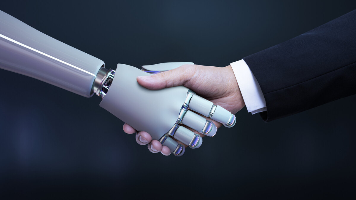 Como Usar a Inteligência Artificial? 7 Dicas Valiosas Para o Seu Negócio 2 Uma imagem próxima de um aperto de mãos entre uma mão humana, vestida com um terno escuro, e uma mão robótica de cor clara e design futurista. A mão humana é visivelmente real, enquanto a mão do robô possui articulações metálicas e um acabamento liso, simbolizando a interação e colaboração entre humanos e a Inteligência Artificial.
