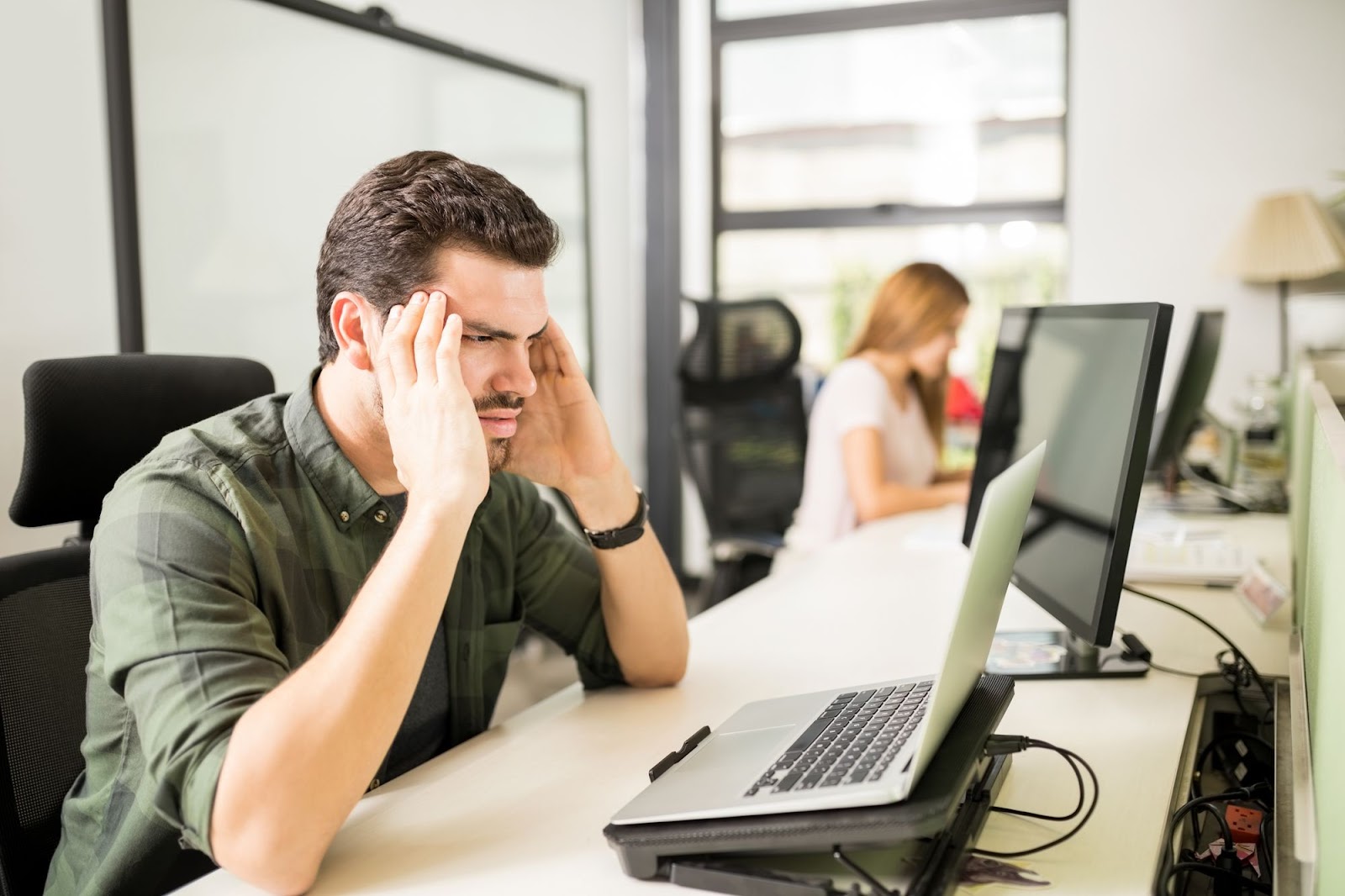 Funil de Quiz: Como Transformar seu Quiz em uma Máquina de Leads Qualificados e Aumentar suas Vendas 5 Um homem com uma expressão de frustração apoia a cabeça com as mãos enquanto olha para um laptop em uma mesa de escritório, representando as dificuldades que podem surgir ao implementar ou otimizar um funil de quiz.