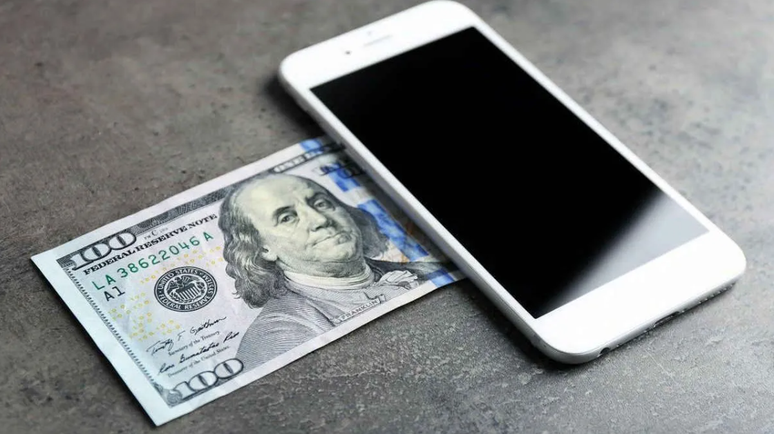 Vender Pelo WhatsApp Funciona Mesmo ou é Só Mais uma Moda? 3 $100 em notas de dólar parcialmente cobertos por um smartphone branco, simbolizando a forma como é possível vender pelo WhatsApp e ganhar dinheiro.